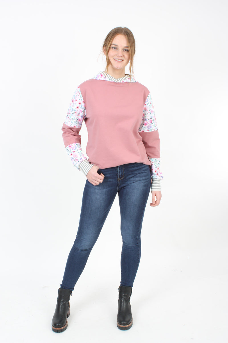 A Women wearing a pink and floral  sweat shirting Hoodie, with denim jeans.